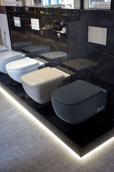 a bathroom with black marble walls and flooring, three toilets are on display in front of the mirror