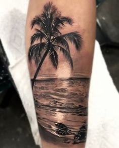 a man's arm with a palm tree and ocean scene on it, while the sun is setting