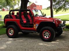 a red jeep is parked under a tree