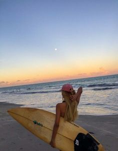 a woman sitting on top of a surfboard next to the ocean in front of a sunset