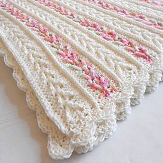 a white crocheted blanket with pink and green flowers on it sitting on a table