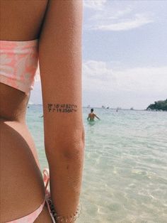 a woman with a tattoo on her arm standing in front of the ocean while another person swims in the water