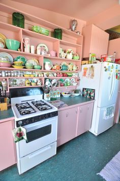 a kitchen with pink cabinets and white stove top oven next to shelves filled with dishes