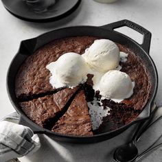 a chocolate cake with ice cream on top in a skillet next to two spoons