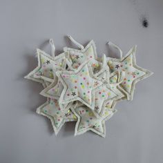 several white and multicolored stars hanging from strings on a gray wall, with one star shaped like an ornament in the middle