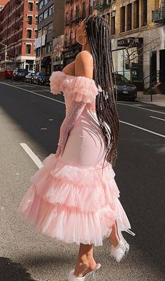 a woman in a pink dress is walking down the street with her long hair pulled back