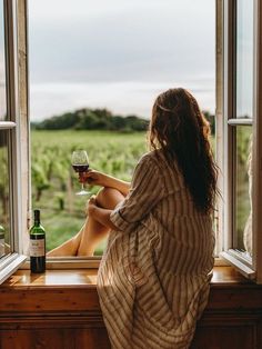 a woman sitting on a window sill with a glass of wine in her hand