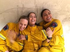 three women in yellow fire suits are smiling and hugging each other with their arms around one another