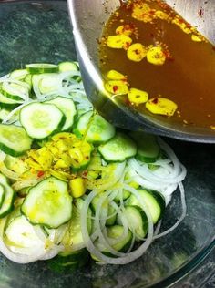 sliced cucumbers and onions in a bowl with oil being poured over them on the side