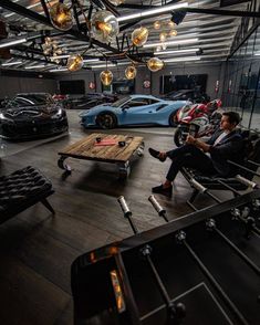 a man sitting in a chair next to a table with cars on it and chandeliers hanging from the ceiling