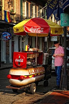 a man standing in front of a hot dog cart on the side of a street