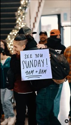 two people hug each other while holding a sign that says see you sunday sam and i am