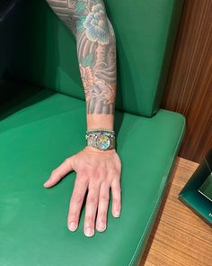 a man with tattoos on his arm and wrist sitting in a green chair next to a book