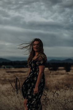 a woman standing in the middle of a field with her hair blowing in the wind