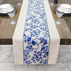 a blue and white floral table runner on a wooden table with place settings in front of it