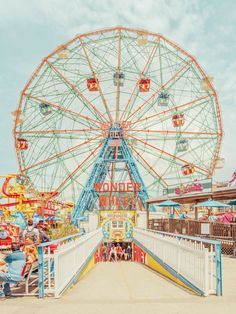 an amusement park with ferris wheel and people sitting on the bench at the entrance to the ride