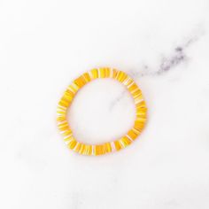 a yellow beaded bracelet sitting on top of a white marble countertop next to an orange flower