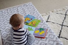 a toddler sitting on the floor with books in front of him and looking at them