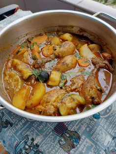 a pot filled with stew and potatoes on top of a tablecloth covered table next to a window