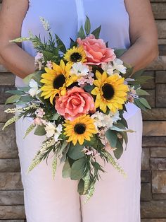 a woman holding a bouquet of sunflowers and roses in front of a brick wall