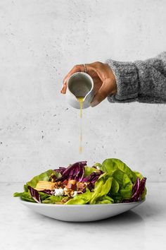 someone pouring dressing onto a salad in a white bowl