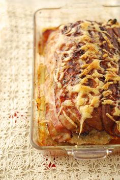 a casserole dish with meat and cheese in it on a lace tablecloth