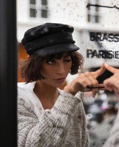 a woman wearing a black hat is looking at her cell phone while another person stands in the background