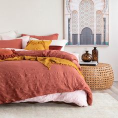 a bed with orange and white pillows in a bedroom next to a painting on the wall