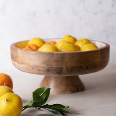 a wooden bowl filled with lemons and oranges on top of a white table