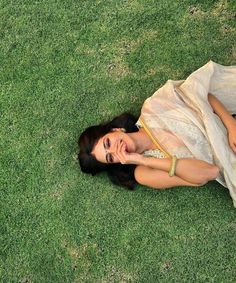 a woman laying in the grass with her hand on her face and looking up at something