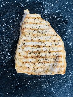 a piece of grilled meat sitting on top of a black surface covered in salt and pepper