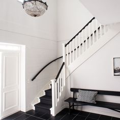 a black and white entryway with a bench under the stairs, and a chandelier hanging from the ceiling