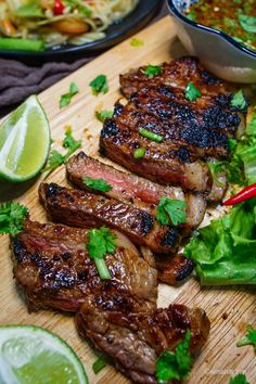 some steaks are on a cutting board with vegetables and lime wedges next to them