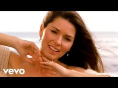 a woman is smiling and holding something in her hand while standing on the beach near the ocean