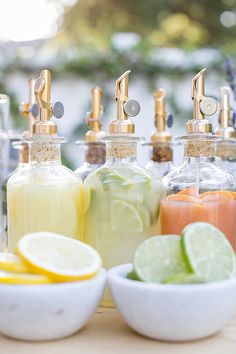 bottles filled with different types of liquid sitting on top of a wooden table next to lemons and limes