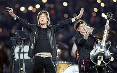 the rolling stones performing on stage with their hands in the air and two guitars behind them