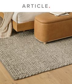 a bed with a brown footstool sitting next to it on top of a wooden floor