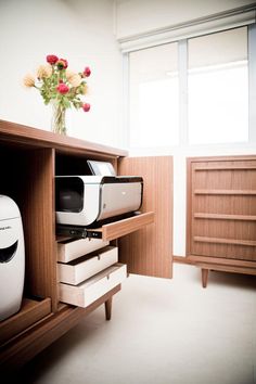 a white printer sitting on top of a wooden cabinet next to a vase with flowers