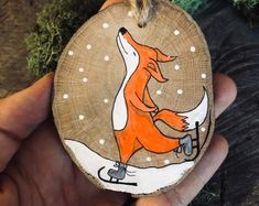 a hand holding a wooden ornament with an image of a fox on it