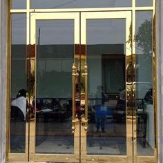 an open glass door on the side of a building with gold trimmings and large windows