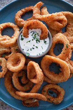 an air fryer onion rings on a blue plate with ranch dip in the middle