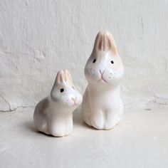 two ceramic rabbits sitting next to each other on a white surface with a wall in the background