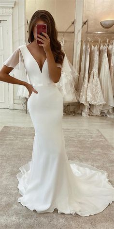 a woman taking a selfie in front of her wedding dress and looking at her phone