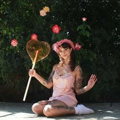 a woman sitting on the ground holding a heart shaped lollipop with her hands