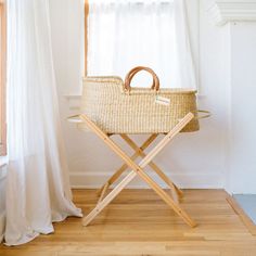 a wicker basket sitting on top of a wooden chair next to a window with white curtains