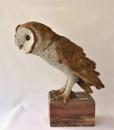 an owl figurine sitting on top of a wooden block with white and brown paint