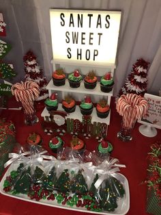 a table topped with lots of cupcakes covered in candy next to christmas trees