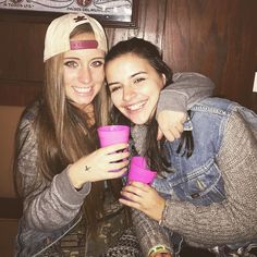 two young women are posing for the camera with cups in front of their faces and one has her arm around another woman's shoulder