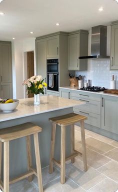 a large kitchen with two stools in front of the counter and an island that has flowers on it