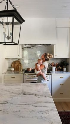 a woman holding a baby in her arms while standing next to a kitchen counter top